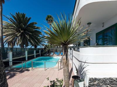 Modern pool area with palm trees beside a white hotel building under clear sky