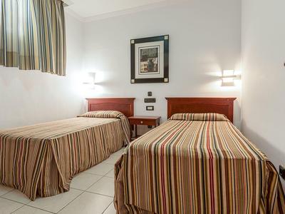 Prosty pokój hotelowy z dwoma pojedynczymi łóżkami i paskowanymi pościelami.