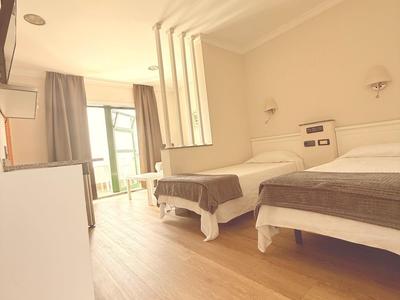 Jasny pokój hotelowy z dwoma łóżkami, drewnianą podłogą i balkonem z widokiem.