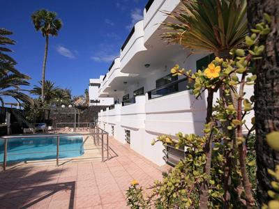 Innenhof eines Hotels mit Pool, Palmen und weißen Gebäuden bei sonnigem Wetter.