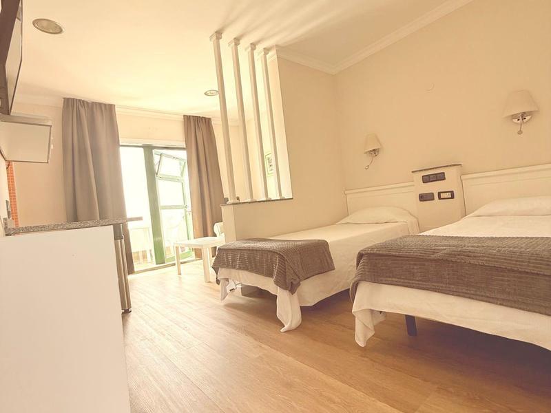 Jasny pokój hotelowy z dwoma łóżkami, drewnianą podłogą i balkonem z widokiem.