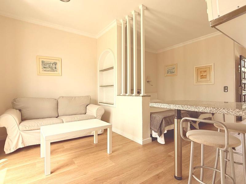 Jasny salon z sofą, białym stolikiem kawowym i barkiem z hokerami.