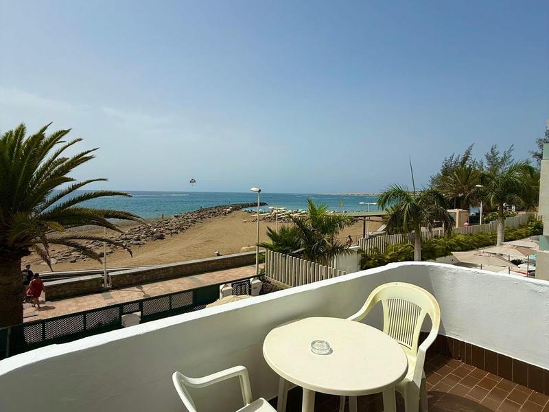 Mały balkon z białym stołem i krzesłami z widokiem na plażę i morze.