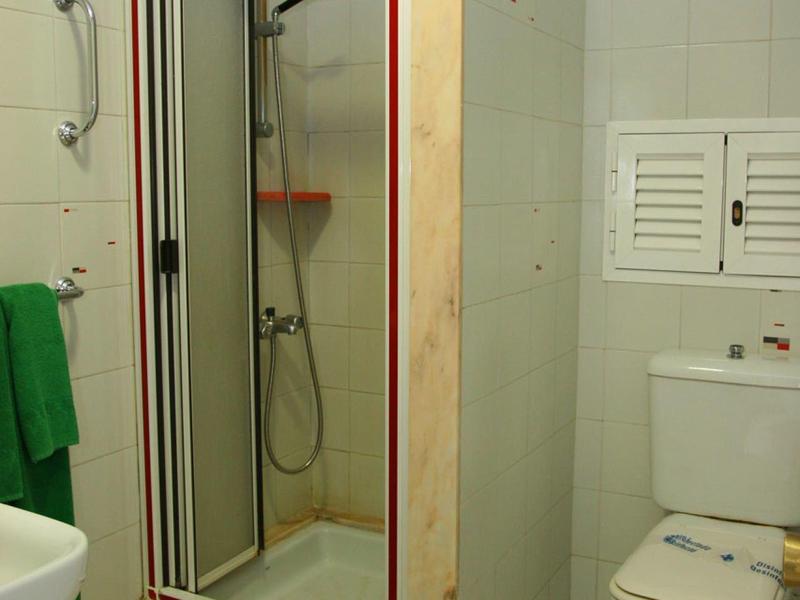 Mała kabina prysznicowa z drzwiami szklanymi, słuchawką prysznicową, toaletą i białymi płytkami.