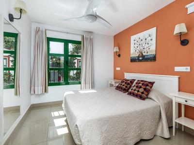 Helles Schlafzimmer mit weißem Bett, orangefarbener Wand und grünem Fensterrahmen.