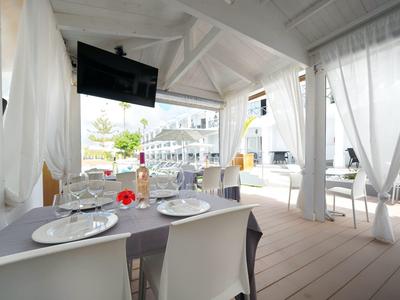 Hell eingerichtete Terrasse mit weißem Dach, Vorhängen und gedecktem Tisch mit Gläsern und Tellern.