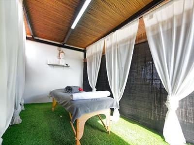 Hell eingerichteter Massagebereich mit Holztisch, weißen Vorhängen und grünem Teppichboden.