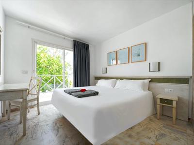 Helles Schlafzimmer mit Doppelbett, Holzmöbeln, großen Fenstern und Balkon mit grünem Blick.