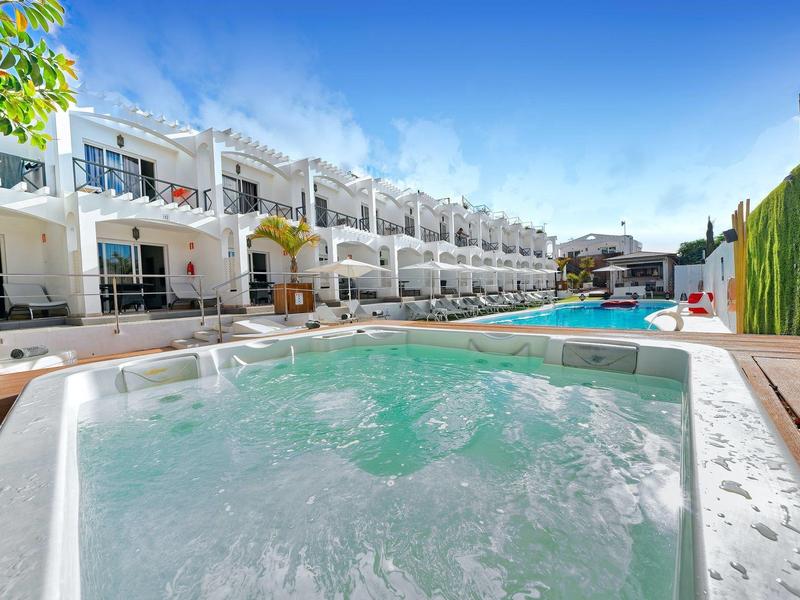 Moderner Außenbereich mit Whirlpool und großem Pool, weißen Gebäuden und blauem Himmel.