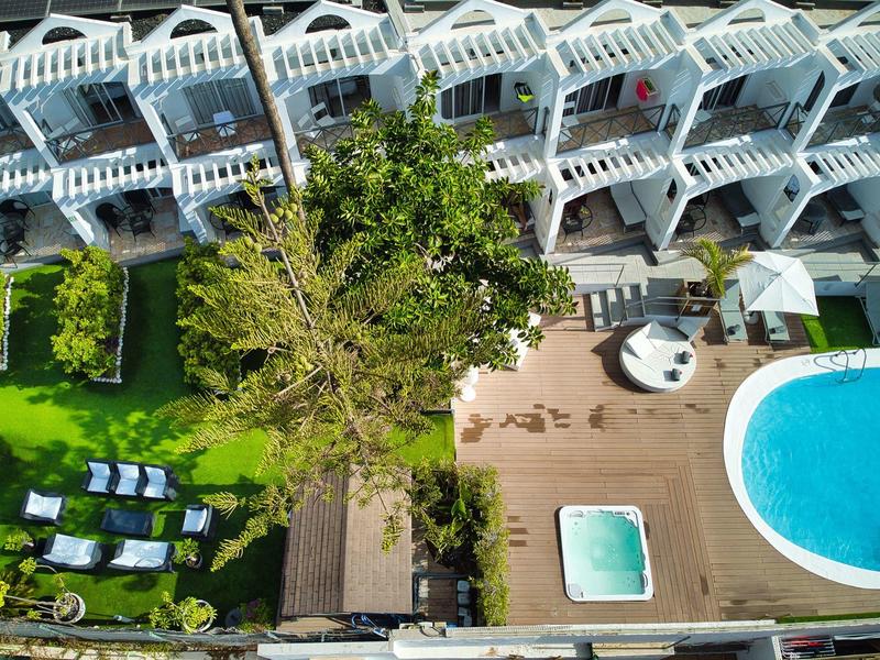 Überblick eines Hotels mit Pool, Sonnenterrasse, grünen Liegen und mehrstöckigem Balkon in Reihenform.