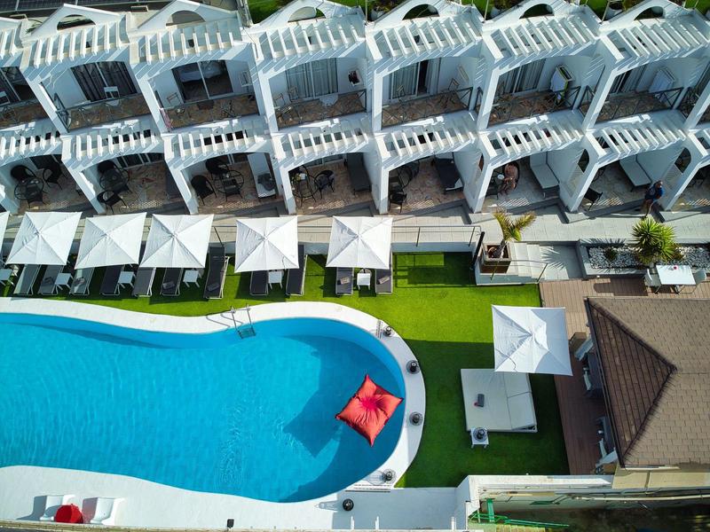 Großer blauer Pool mit Sonnenschirmen, weißen Liegestühlen und grünem Rasen daneben.