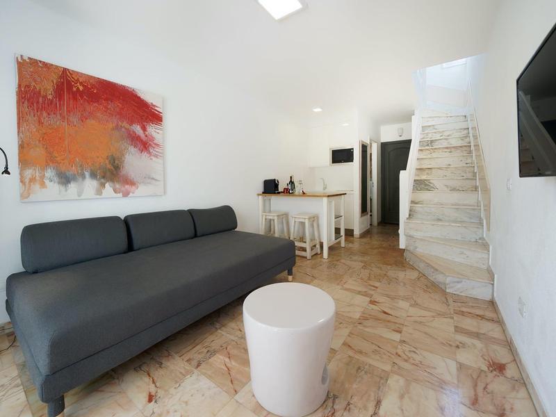 Moderner Wohnraum mit grauem Sofa, rundem weißen Tisch, abstraktem Bild und weißer Treppe.