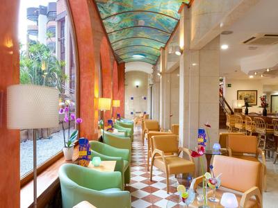 Interno elegante di un hotel con poltrone colorate e soffitto dipinto sotto una finestra a volta.
