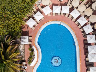 Round pool with white sun loungers and tables, surrounded by plants and red pavement