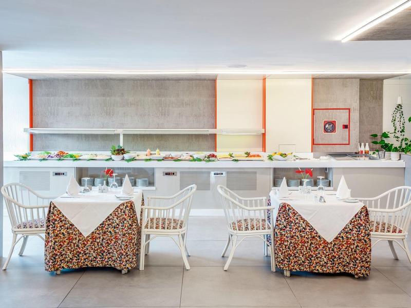 Zona pranzo moderna con sedie bianche e coperture decorate davanti a un lungo tavolo buffet con cibo.