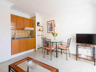 Malá kuchyňka s dřevěnými skříňkami a přilehlou jídelní částí se skleněnou deskou a černým kovovým rámem.