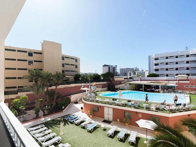 Venkovní prostor hotelu s kulatým bazénem, lehátky a několika budovami v pozadí.