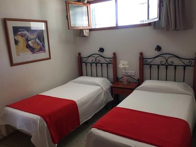 Dvoulůžkový pokoj s bílým povlečením a červenými přikrývkami, obraz na stěně a otevřené okno.