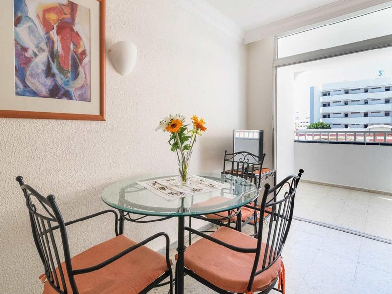 Moderní jídelní prostor se skleněným stolem a čtyřmi kovovými židlemi vedle hotelového balkonu.