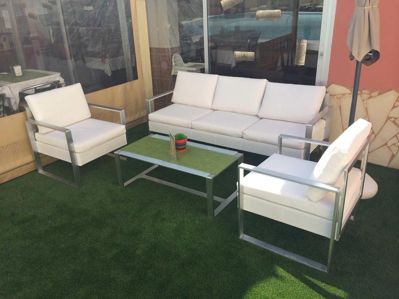 Moderní posezení s pohovkou a křesly na umělé trávě vedle skleněných stěn a slunečníku.