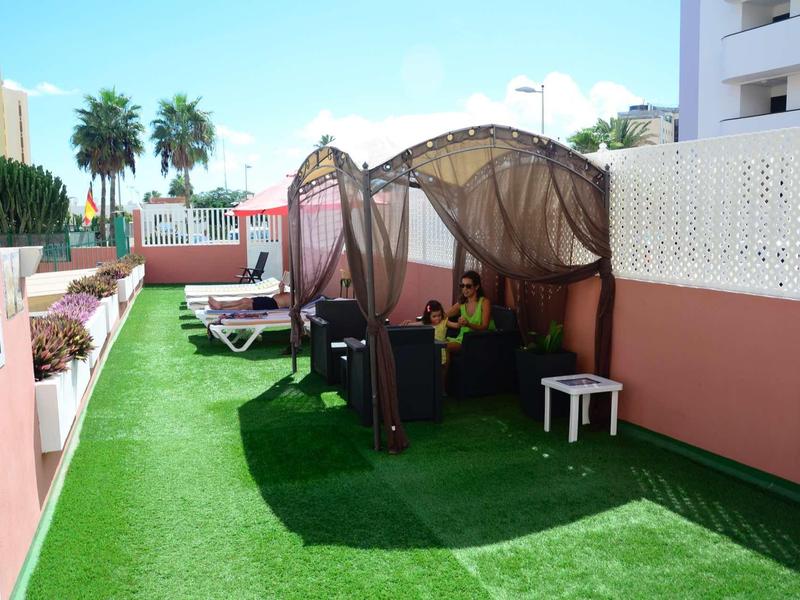 Hotelová terasa s lehátky, altánky a umělým trávníkem pod jasnou oblohou.