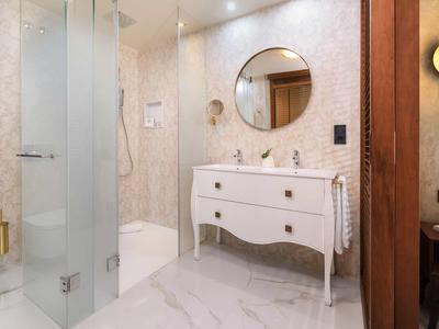 Nowoczesna łazienka z prysznicem, umywalką na białej szafce i okrągłym lustrem.