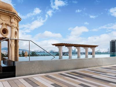 Przestronny taras z drewnianą podłogą, widok na basen i miejską panoramę pod błękitnym niebem.