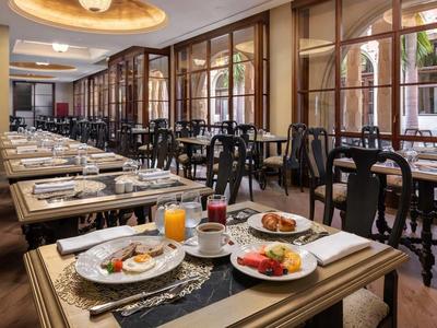 Elegancka jadalnia hotelowa z nakrytymi stołami i widokiem na ogród wewnętrzny.