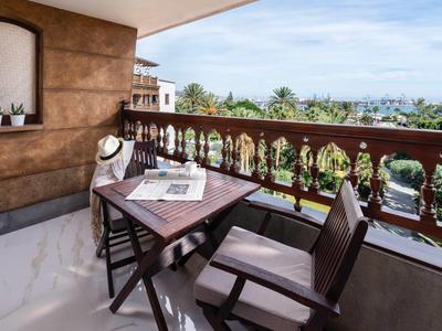 Balkon hotelowy z stołem, krzesłem i widokiem na morze oraz roślinność.