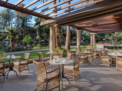 Taras restauracyjny hotelu z szklanymi stolikami i wiklinowymi krzesłami, widok na tropikalny ogród.