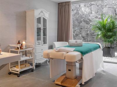 Jasny pokój spa z łóżkiem do masażu przy oknie z widokiem na ogród.