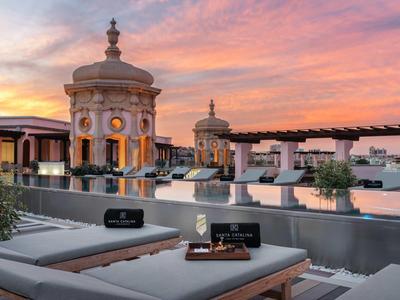 Rooftop terrace with sun loungers and wine in front of a historic building at sunset.