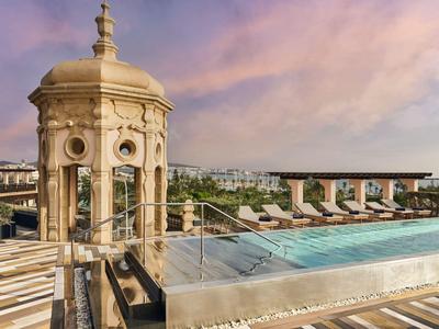 Dachpool mit Liegestühlen und historischer Turmstruktur bei Sonnenuntergang.