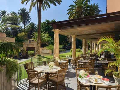 Außenbereich eines Hotels mit gedeckten Tischen, Stühlen und grüner Pflanzenpracht unter Palmen.