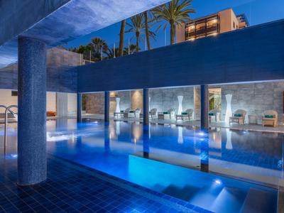 Moderner Hotelpool mit blau beleuchtetem Wasser und gemütlichen Sitzbereichen in der Dämmerung.