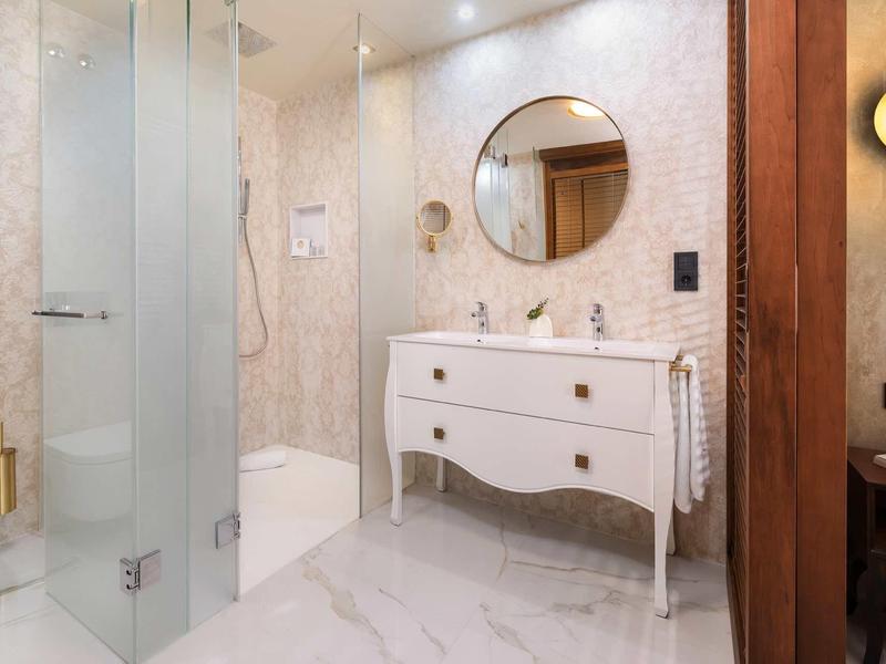 Nowoczesna łazienka z prysznicem, umywalką na białej szafce i okrągłym lustrem.