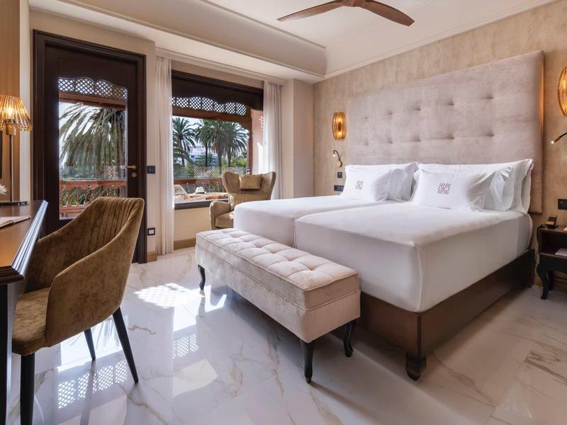 Stylowy pokój hotelowy z podwójnym łóżkiem, aksamitnym krzesłem i balkonem.