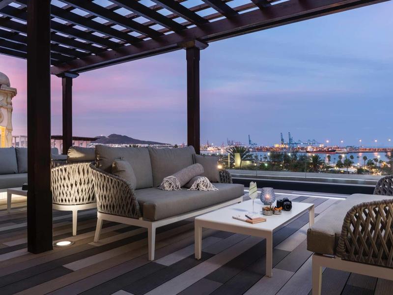 Elegancki taras hotelowy z widokiem na morze o zachodzie słońca, wygodne meble z rattanu.