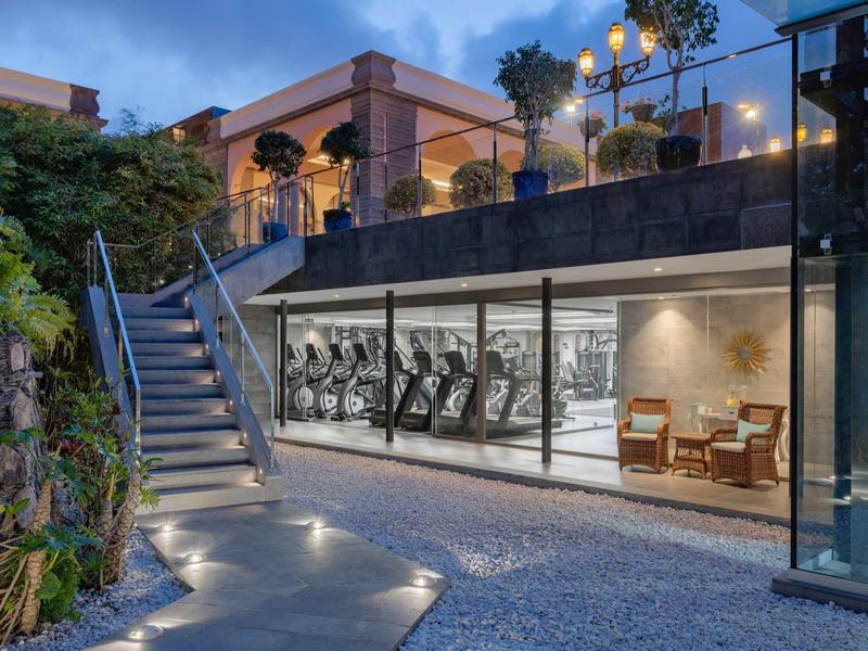Nowoczesna siłownia w podziemiach z eleganckim oświetleniem zewnętrznym i schodami do ogrodu.