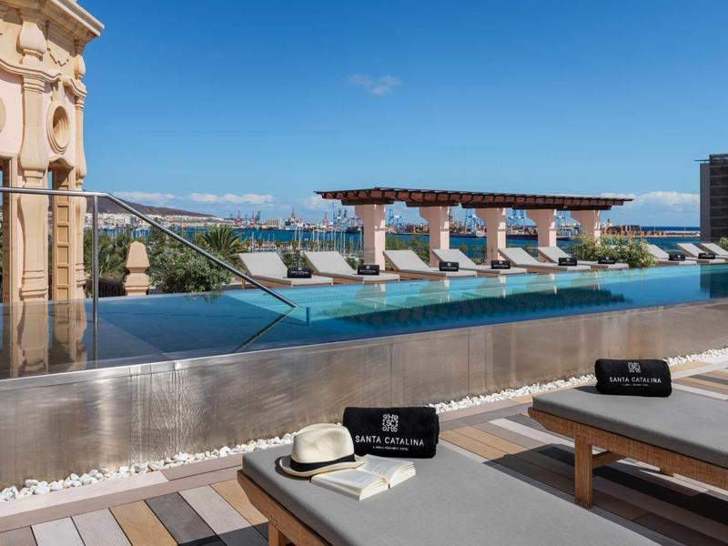 Basen infinity z leżakami i widokiem na miasto i morze w oddali.