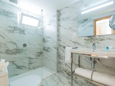 Moderne badkamer met marmeren tegels, glazen douche en een open wastafel met handdoeken.