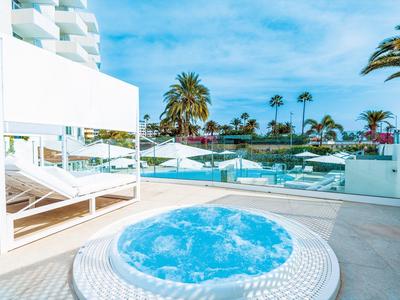 Bubbelbad op een lichte terras met uitzicht op palmbomen en blauwe lucht.