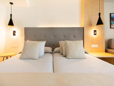 Moderne hotelkamer met twee eenpersoonsbedden, grijze hoofdbord en minimalistisch ontwerp.