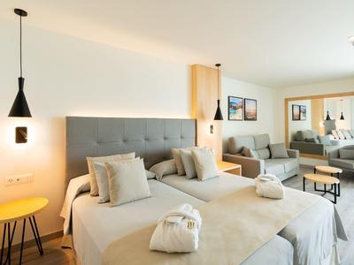 Licht ingericht hotelkamer met twee bedden, zithoek en moderne verlichting.