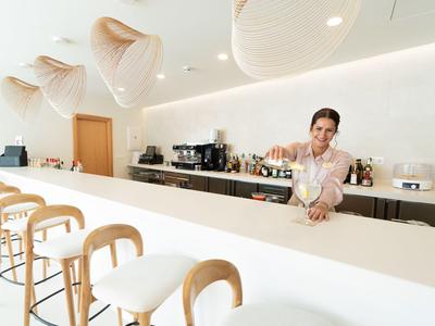 Moderne lichte hotelbar met toonbank, krukken en barkeeper die een drankje inschenkt.