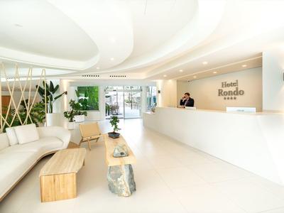Lichte, moderne hotel lobby met witte receptiebalie en houten zithoek met bank.
