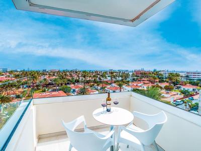 Balkon met witte tafel, twee stoelen, wijn en glazen met uitzicht op een stad en blauwe lucht.