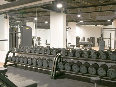 Moderne fitnessruimte met dumbbells en trainingsapparatuur in een lichte, ruime omgeving.