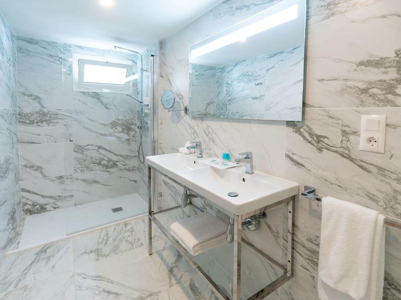 Lichte badkamer met marmeren tegels, grote douche, wastafel met spiegel en handdoekrek.