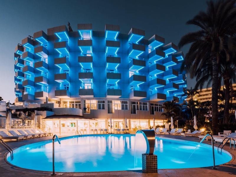 Rond hotel met gloeiende blauwe balkons en verlicht zwembad 's nachts.